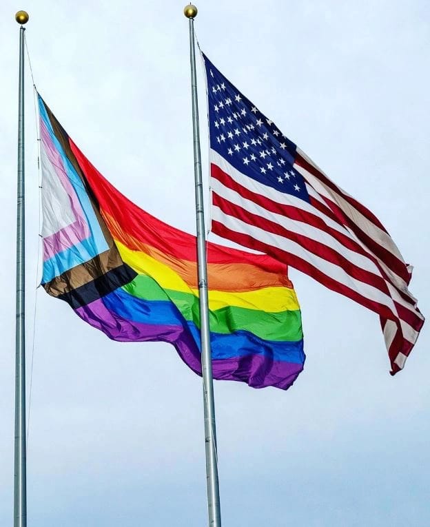 Two flags fly in the wind, one the American Flag one the pride flag